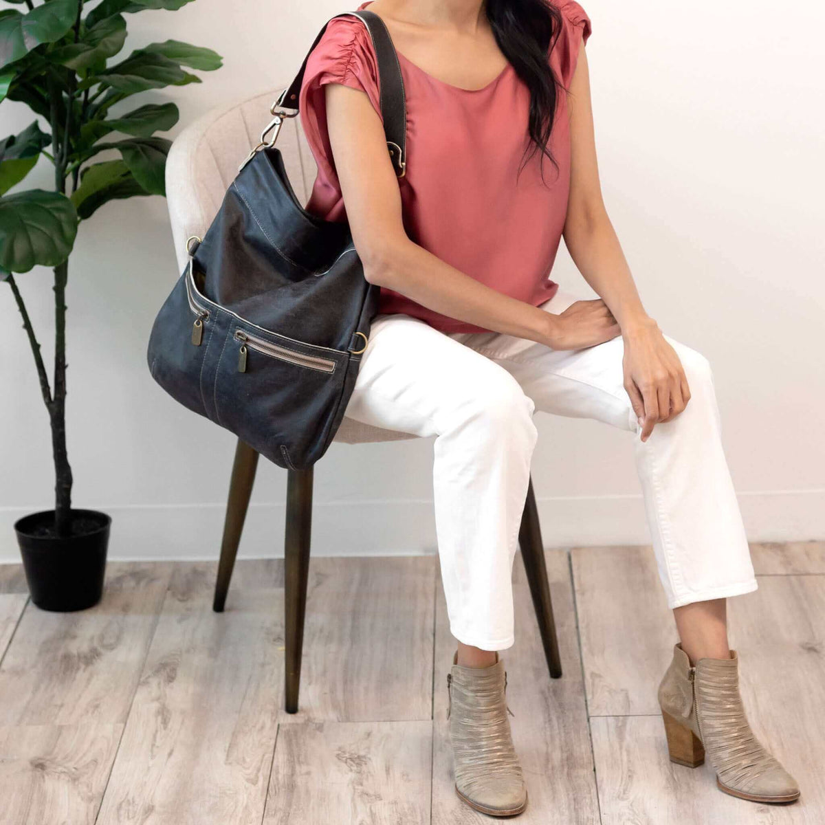 Woman sitting on a chair with an Original Lauren 6-in-1 leather crossbody bag alongside a plant.
