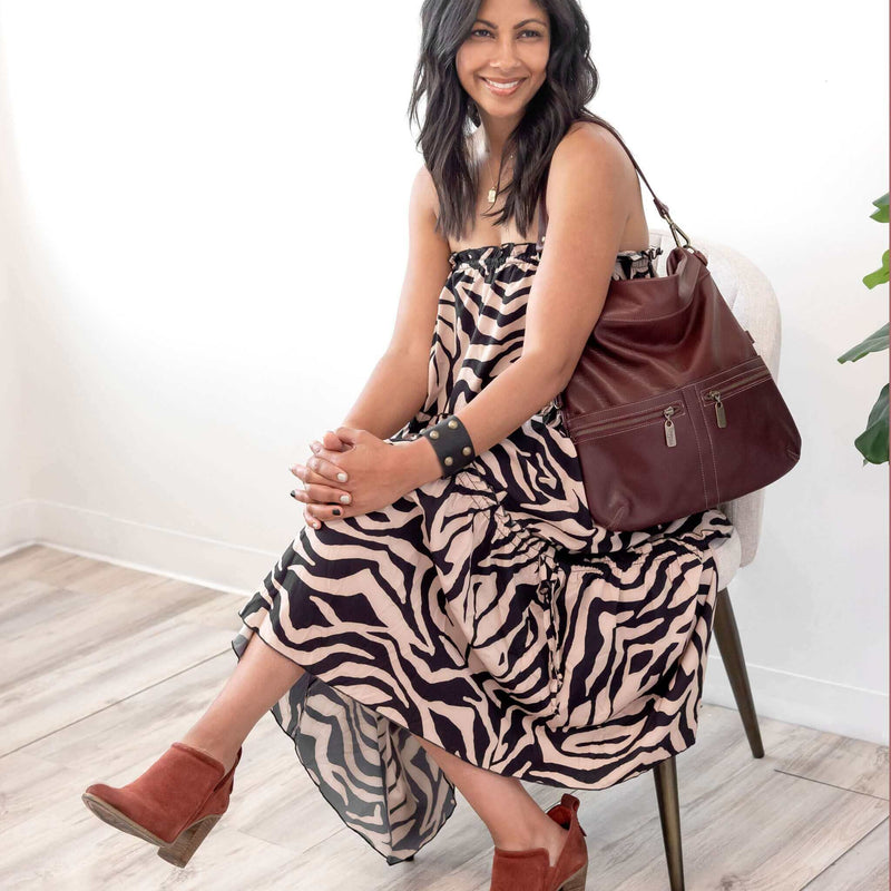 Woman wearing a strapless dress and brown boots, seated with a Mini Lauren 6-in-1 convertible leather crossbody bag in Merlot.