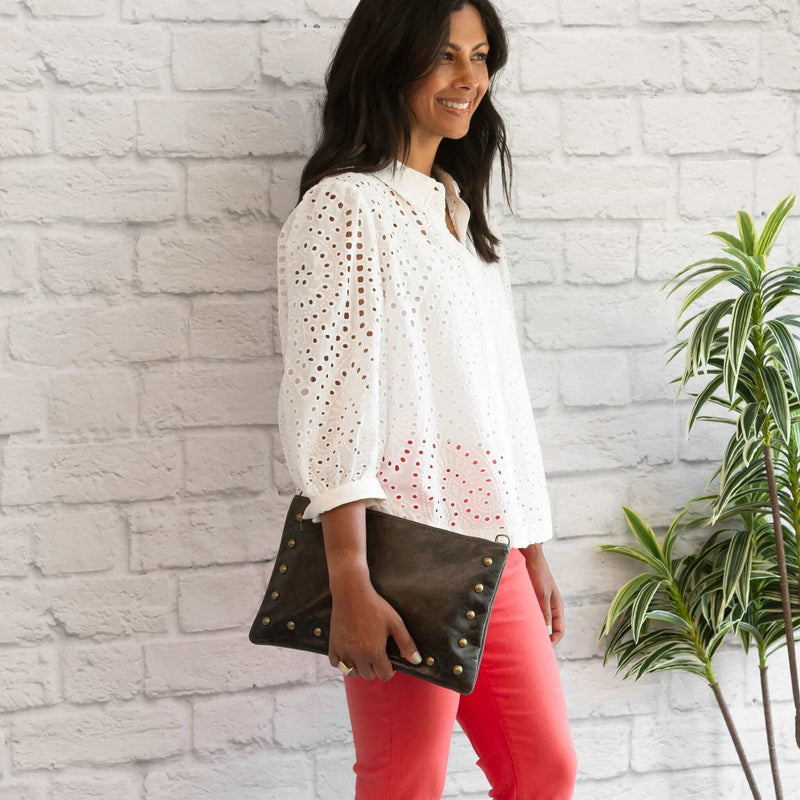 Woman wearing dark charcoal studded crossbody bag in full-grain leather as a clutch