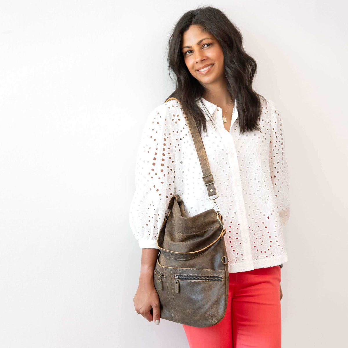 Woman wearing a Mini Lauren leather crossbody bag, showcasing its stylish design with a white blouse and pink pants.