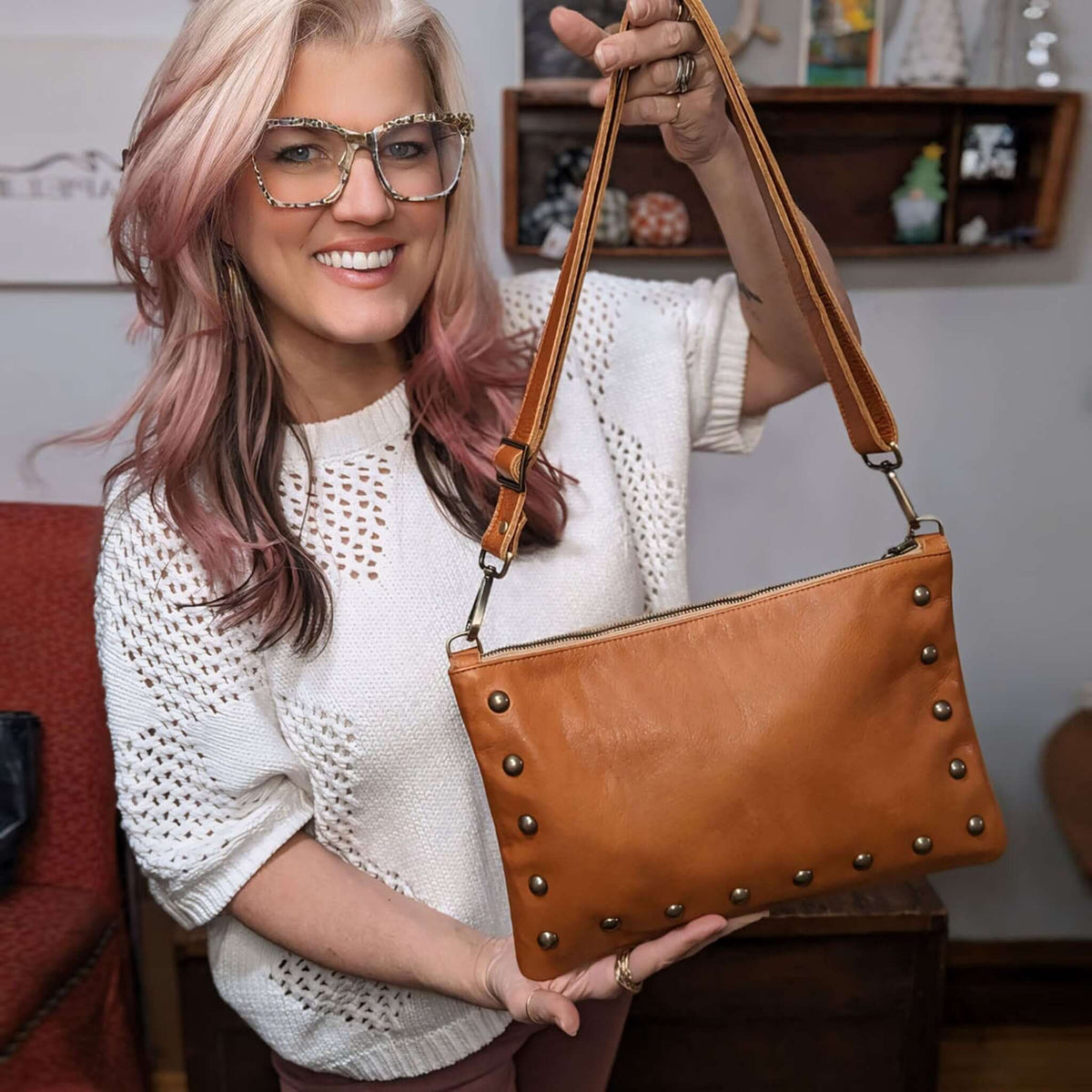 Designer Brynn Capella showcasing our Studded bag in rust full-grain leather convertible clutch-to-crossbody with adjustable strap