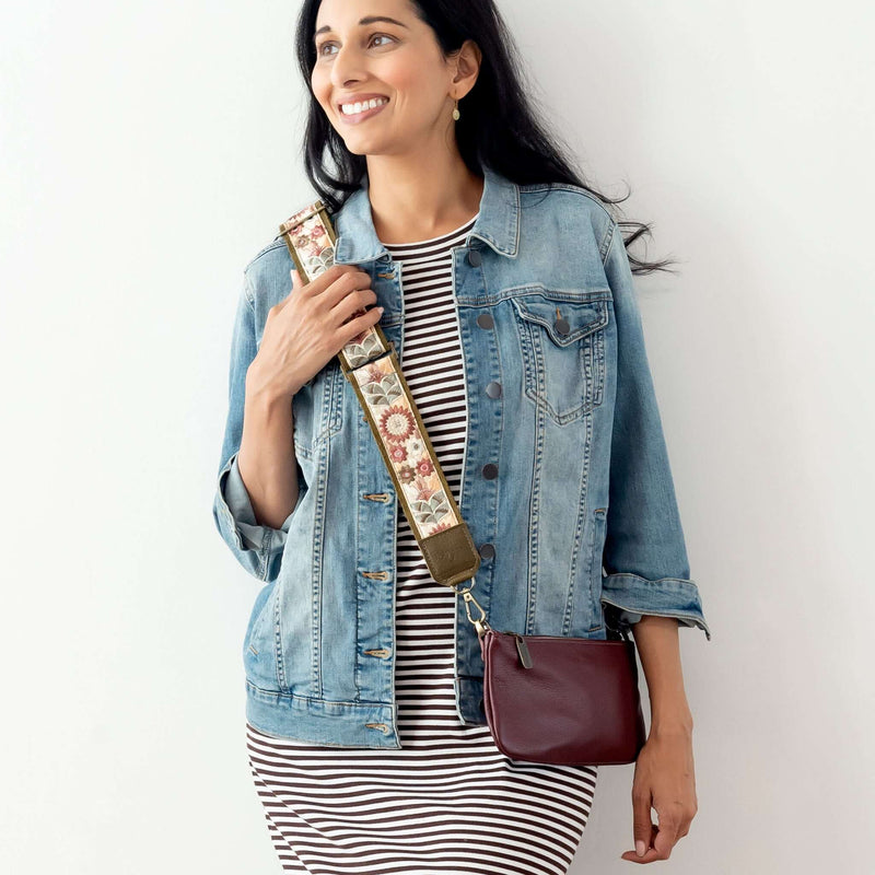 Woman wearing a denim jacket with a floral guitar bag strap while holding a handbag.