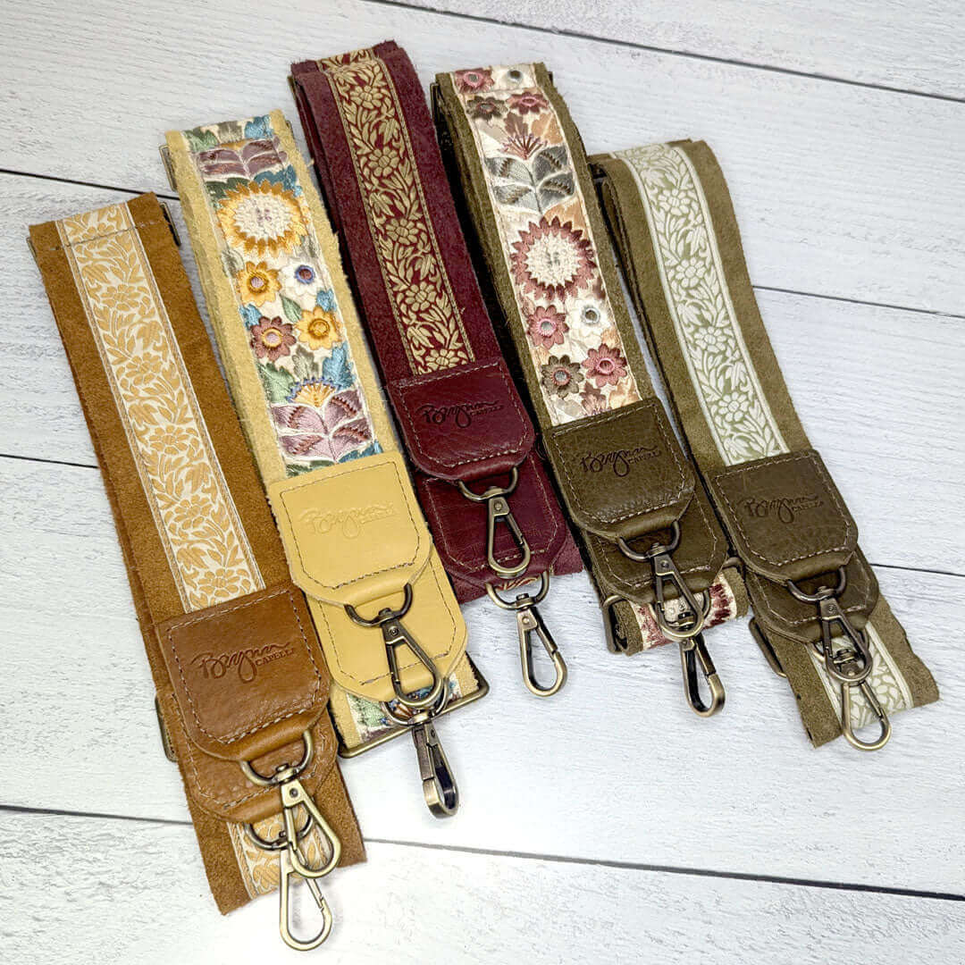 Colorful leather trimmed guitar bag straps in various floral prints on a wooden background.