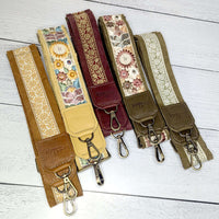 Colorful leather trimmed guitar bag straps in various floral prints on a wooden background.