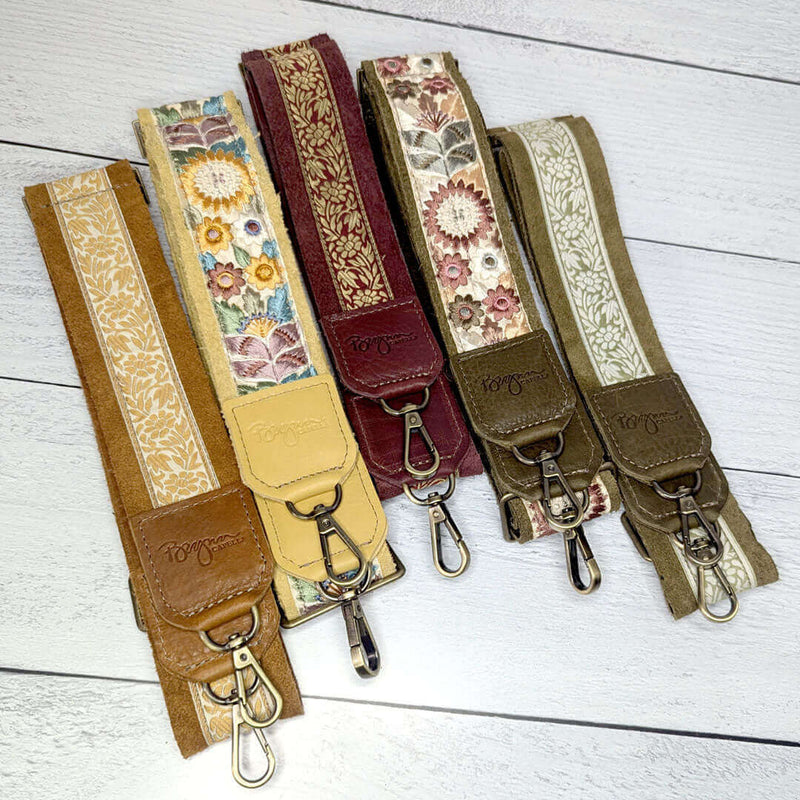 Colorful leather trimmed guitar bag straps in various floral prints on a wooden background.