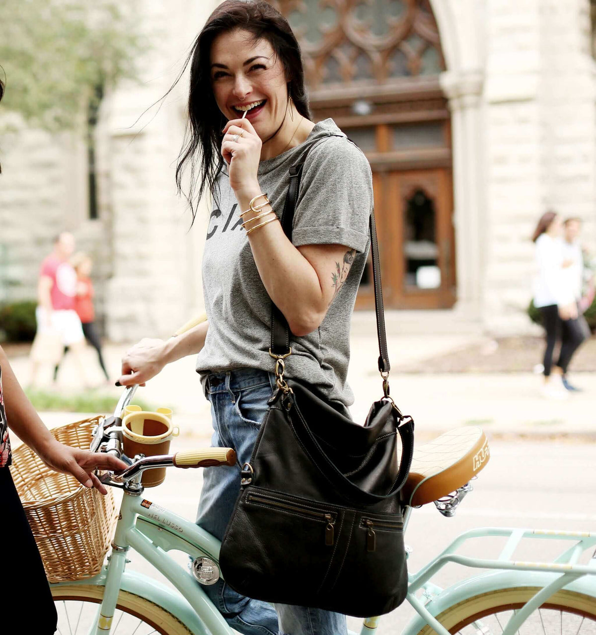 Young woman smiling while riding a bike, showcasing the Original Lauren leather crossbody bag in black sand.