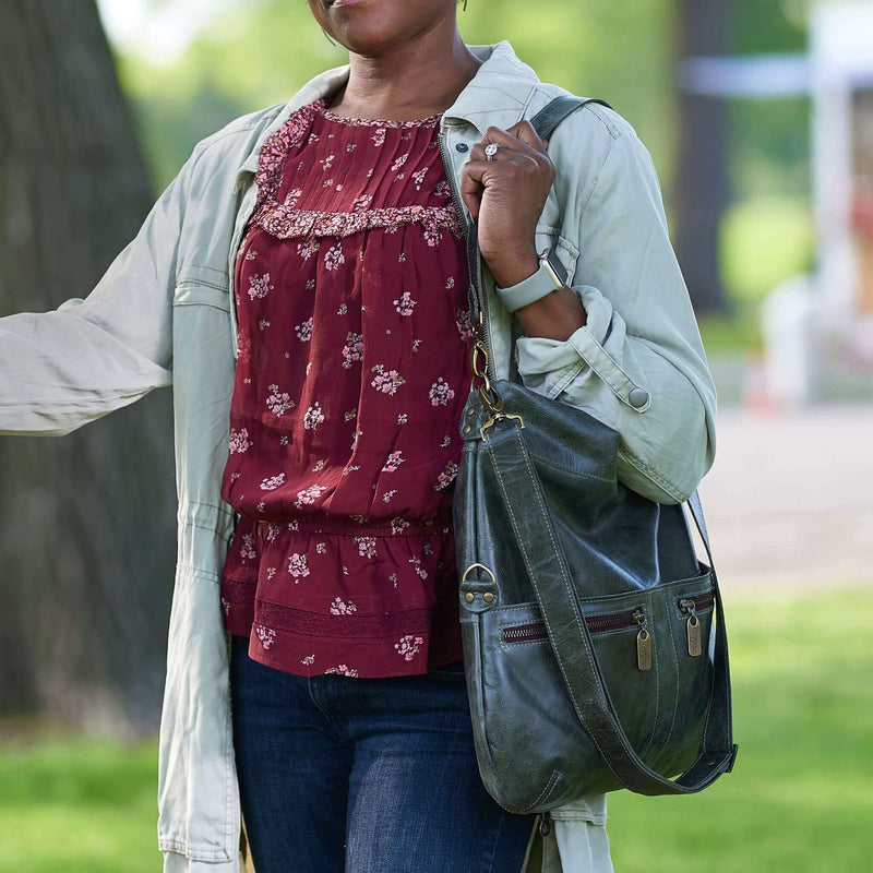Woman wearing a maroon floral top, carrying a Lauren Crossbody - River Rock leather crossbody bags for organized travel.