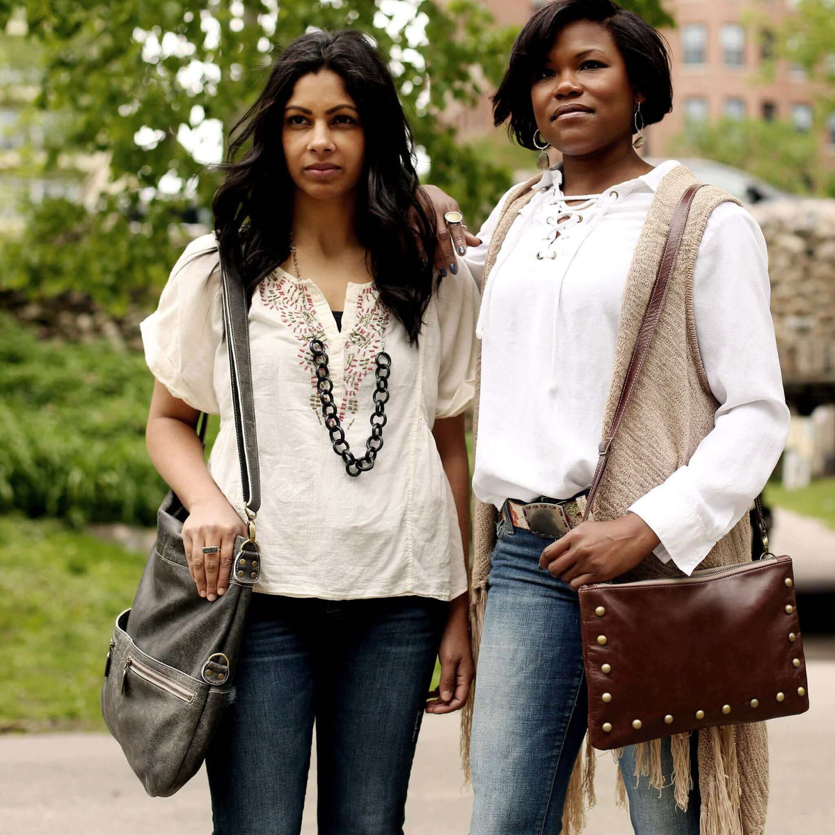 Two women showcasing leather crossbody bags in a casual outdoor setting.