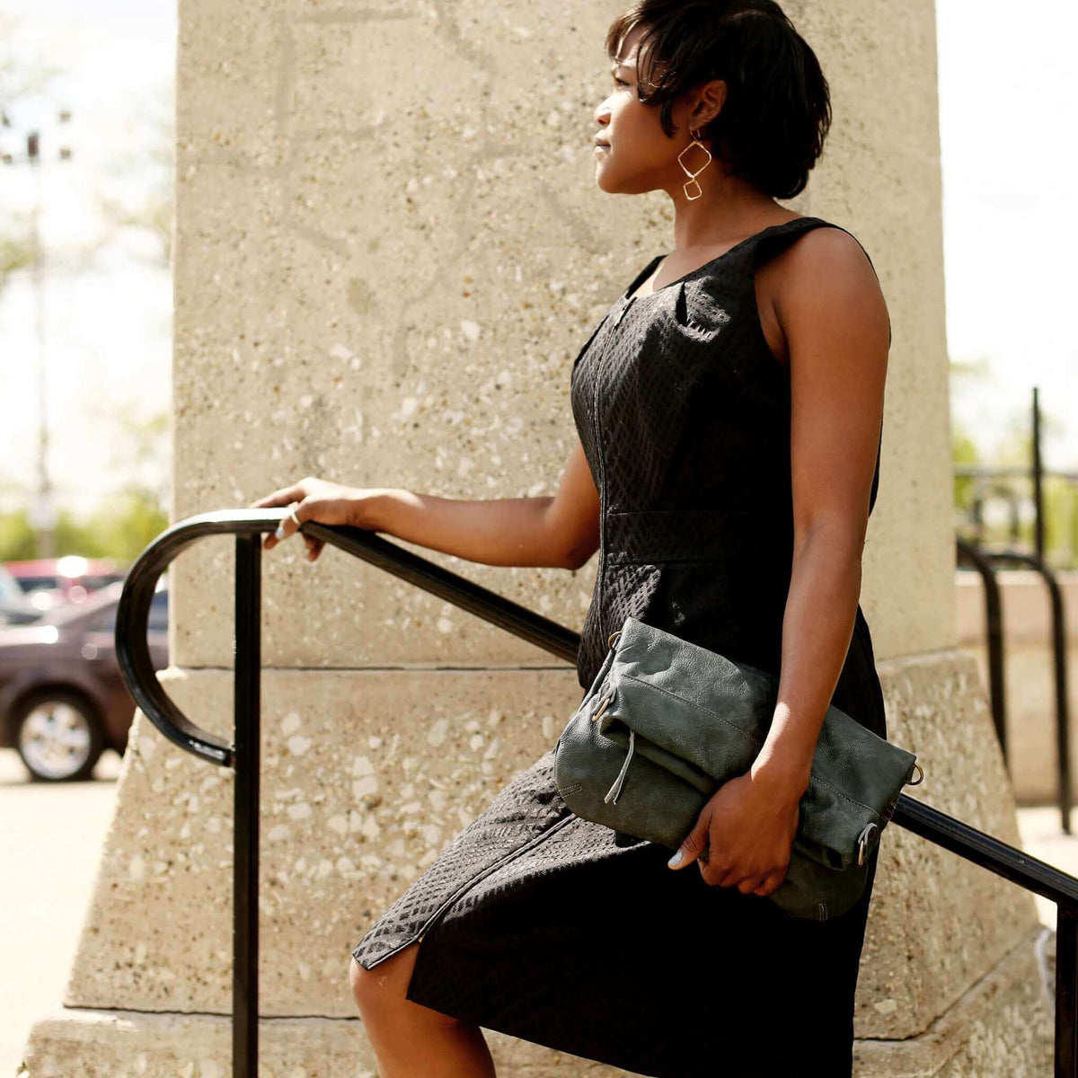 Woman in a black dress holding a Mini Lauren leather crossbody bag while climbing stairs