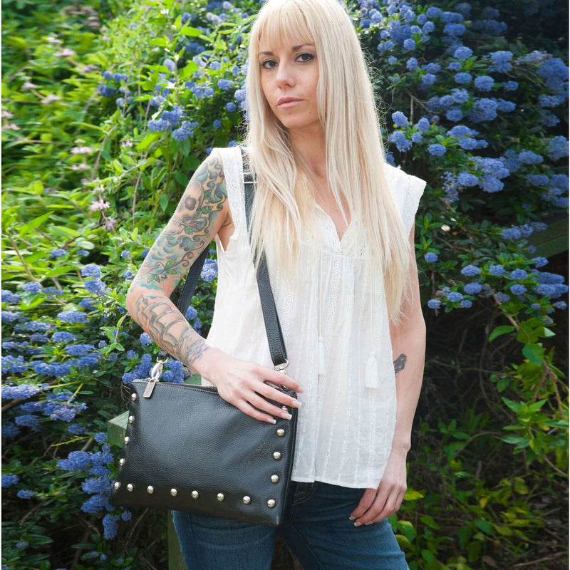 Woman wearing black studded crossbody bag in full-grain leather as a small crossbody bag in the park