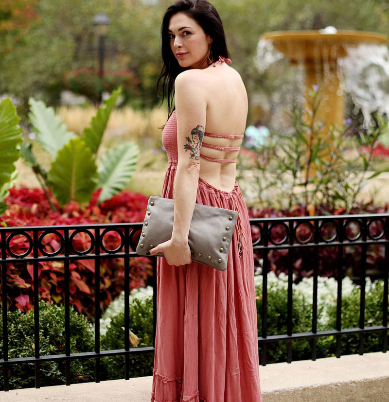 Woman wearing light grey studded crossbody bag in full-grain leather as a clutch in city street