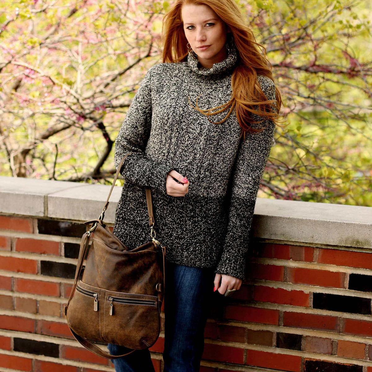 Model wearing a cozy sweater and holding a leather crossbody bag, set against a natural background.