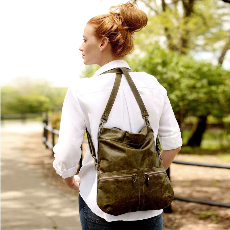 Woman wearing a Mini Lauren leather crossbody bag in olive green as a backpack while walking on a path, showcasing its stylish design.