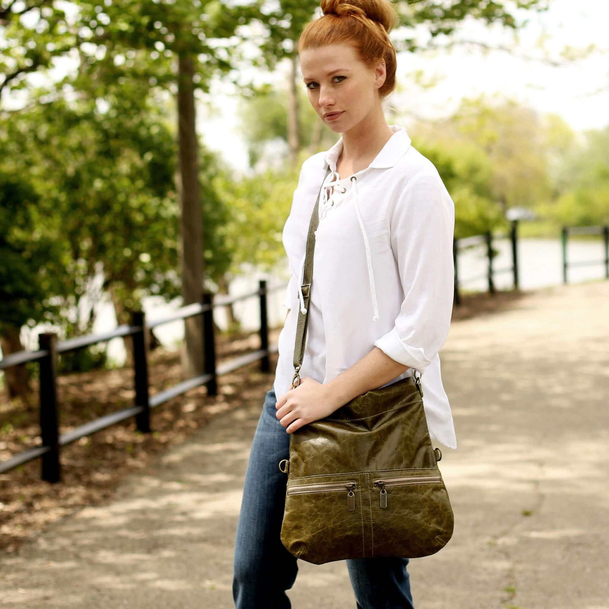 Woman wearing a Mini Lauren leather crossbody bag in olive green while walking on a path, showcasing its stylish design.
